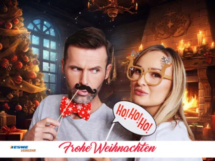 Ein Mann und eine Frau posieren mit weihnachtlichen Requisiten vor einem KI-generierten Kamin-Hintergrund und haben Spaß an der Fotobox auf einem Firmenevent. Das Foto ist mit einem ESWE Verkehr Logo und einem "Frohe Weihnachten"-Schriftzug versehen.